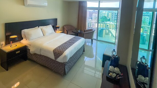 A hotel room with a large bed, a desk, a chair, and a view of the city through large windows. - Dweik Hotel 2 (Aqaba)