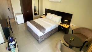 A hotel room with a bed, bedside table with lamp, chair, and a small table with a plant. - Dweik Hotel 2 (Aqaba)