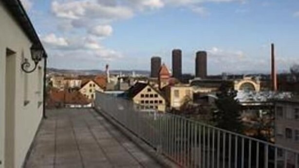 Balkon med udsigt til industribygninger og en klar himmel.