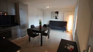 Et moderne køkken med hvide skabe, et spisebord med stole og en grå sofa i opholdsstuen.