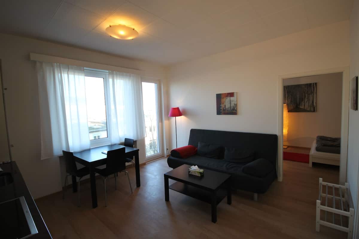 A living room with a dark sofa, a coffee table, a dining table with chairs, and a red floor lamp.