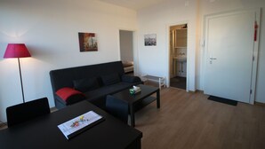 En moderne stue med en sort sofa, et sofabord og en rød lampe. Der er en dør, der fører til et badeværelse og en gang.