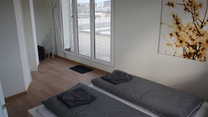 Et værelse med to senge, et vindue med byudsigt, en dørmåtte og et knagered.