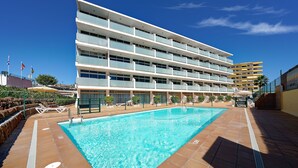 Een hotel met een zwembad, meerdere balkons en een helderblauwe lucht.