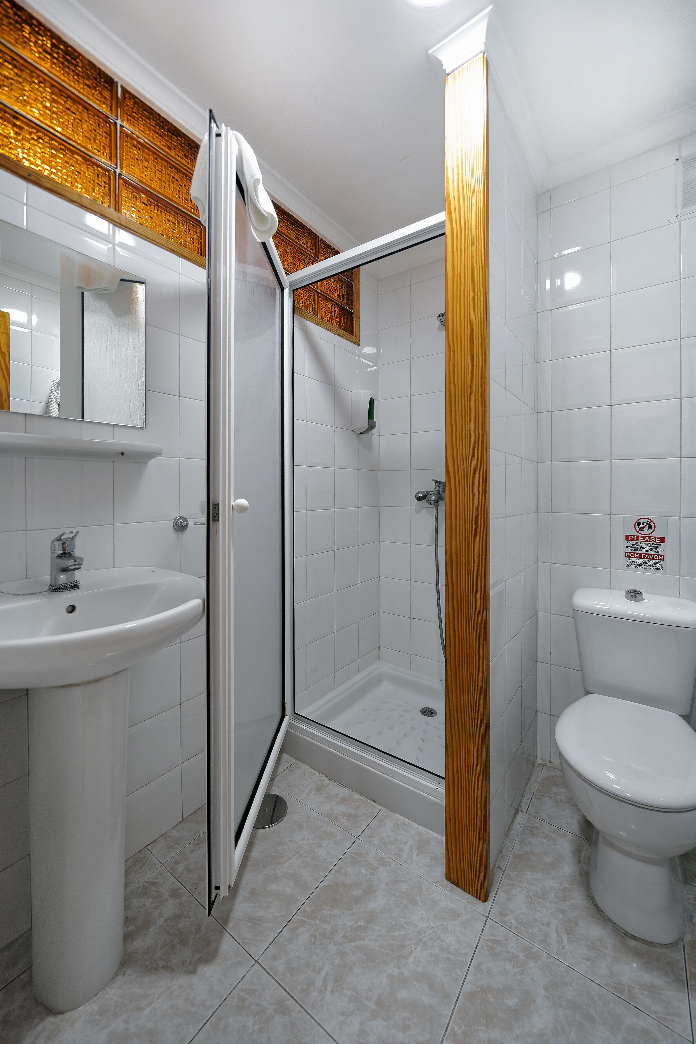 Un baño con cabina de ducha de vidrio, un lavamanos y un inodoro.