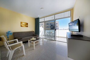 A modern living room with a sofa, a coffee table, a TV, and a fan. - Strelitzias Apartments (San Bartolomé de Tirajana)