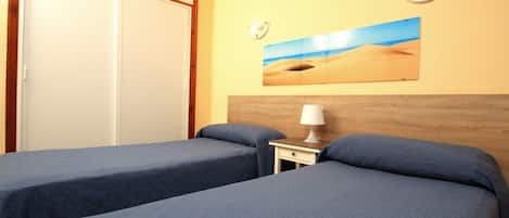 Una habitación de hotel con dos camas individuales, un cabecero de madera, una mesita de noche con una lámpara y un cuadro de paisaje desértico en la pared.