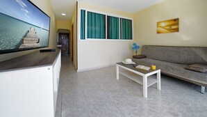 Een woonkamer met een televisie, een bank, een salontafel en een raam met gordijnen.