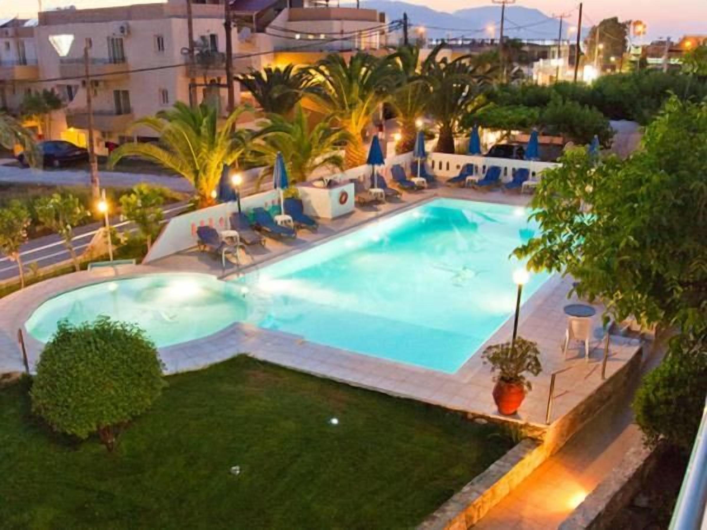 A swimming pool with lounge chairs and umbrellas, surrounded by greenery and buildings.