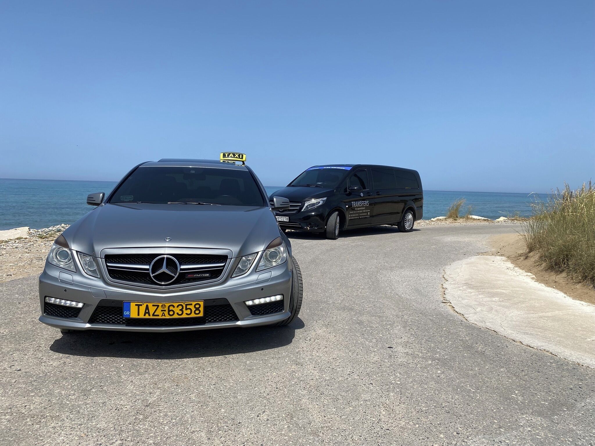 Um Mercedes-Benz prata com placa de táxi e uma carrinha preta com a inscrição 