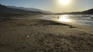 A beach with mountains in the background and the sun setting over the water. - Anatoli Beach (Apokoronas)