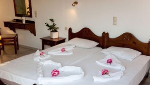 A hotel room with a large bed, a bedside table with a plant, a mirror, and a wooden chair. - Anatoli Beach (Apokoronas)