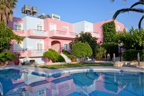 A pink and white building with a swimming pool in the foreground. - Anatoli Beach (Apokoronas)