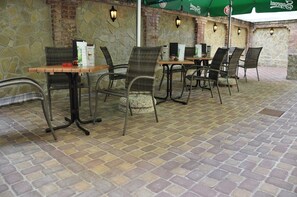 Een terras buiten met stenen muren en een vloer van baksteen, met tafels en stoelen.