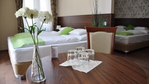 Et hotelværelse med to senge, et træspisebord med en vase med hvide blomster, og et lille bord med fire glas.