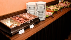 En buffet med flere madstationer, herunder fade med kød og salat samt stakke af tallerkener.
