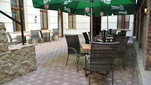 En udendørs terrasse med fletningsmøbler og grønne parasoller, stenmure og en brobelagt gulv.