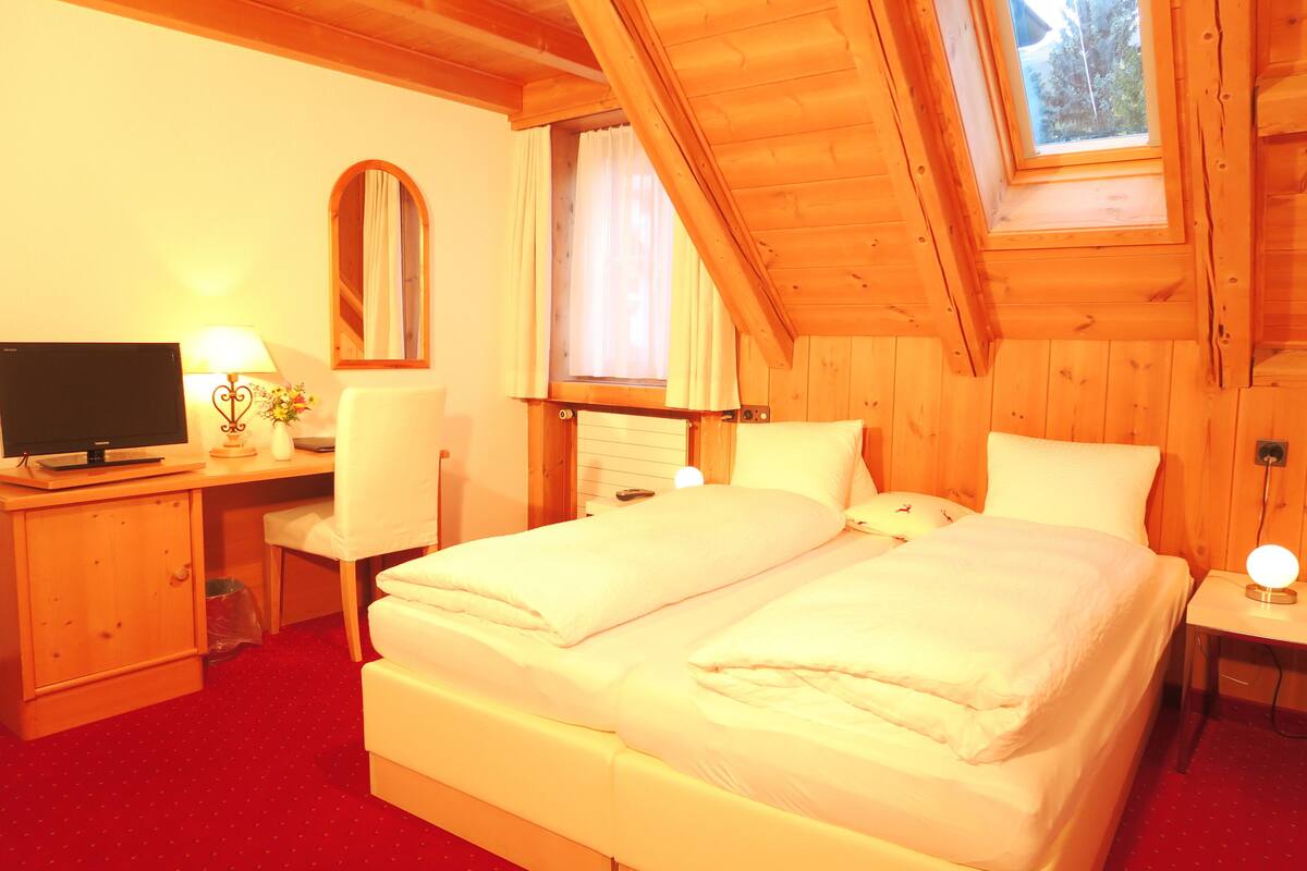 A cozy room with a bed, a desk with a computer, a chair, and a window with curtains.