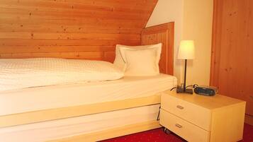 A wooden bunk bed with a white mattress and pillows, a bedside table with a lamp and a radio, and a red carpeted floor.