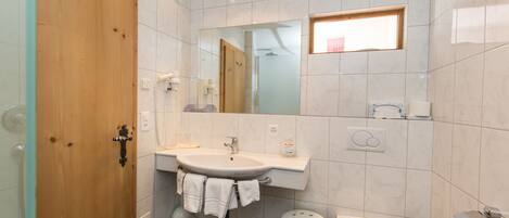 A bathroom with a wooden door, a sink with a mirror above it, a toilet, and a small stool.