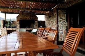 Un espace extérieur aménagé pour les repas, avec un mur en pierre, une table en bois et des chaises.