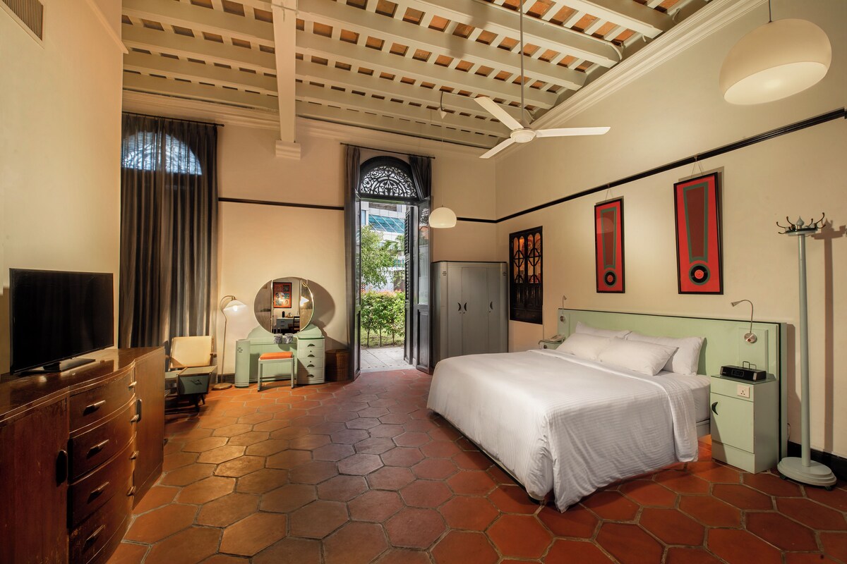 A bedroom with a bed, a desk, a television, and a ceiling fan.