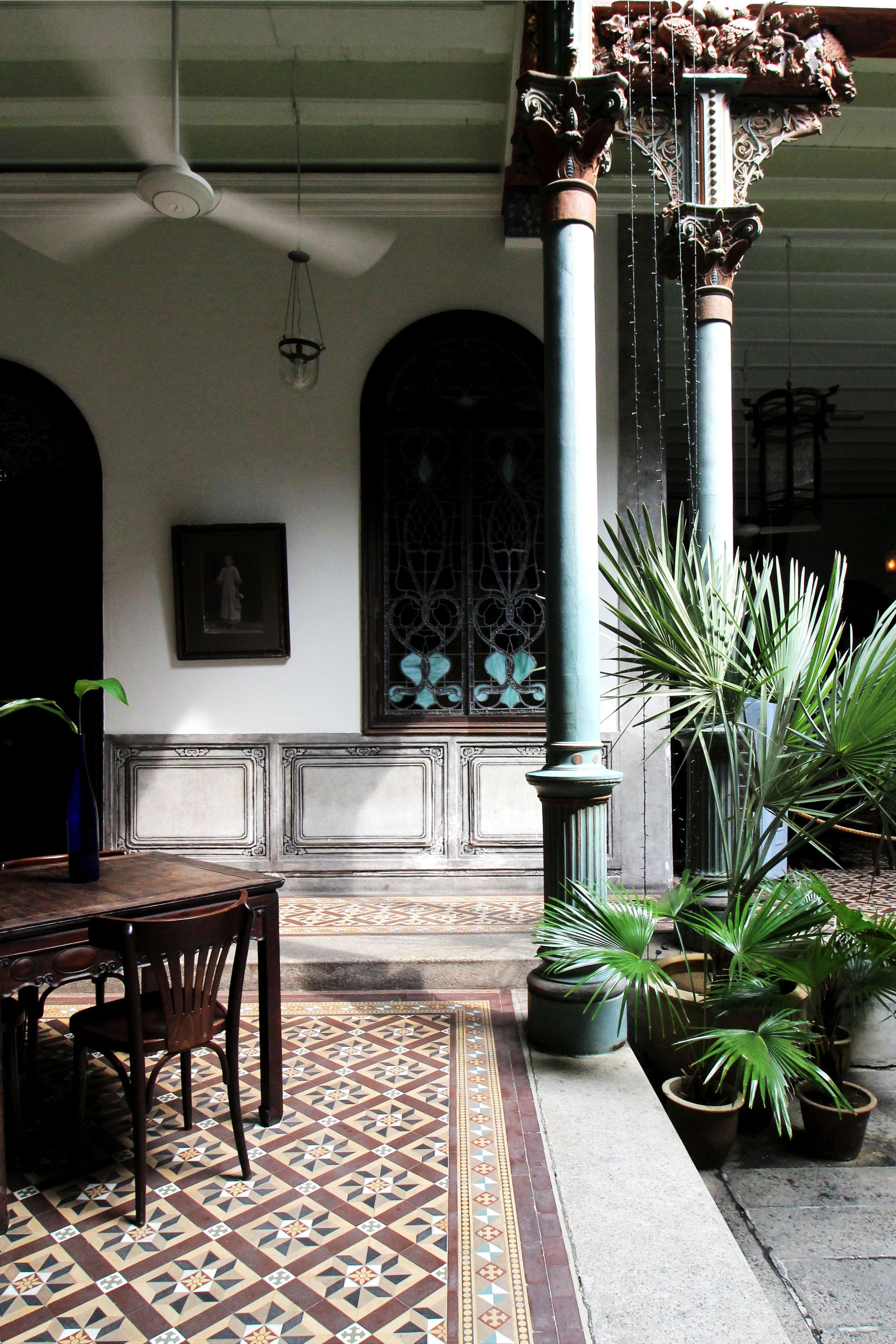 A room with a patterned floor, a table with chairs, a potted plant, and a decorative column.