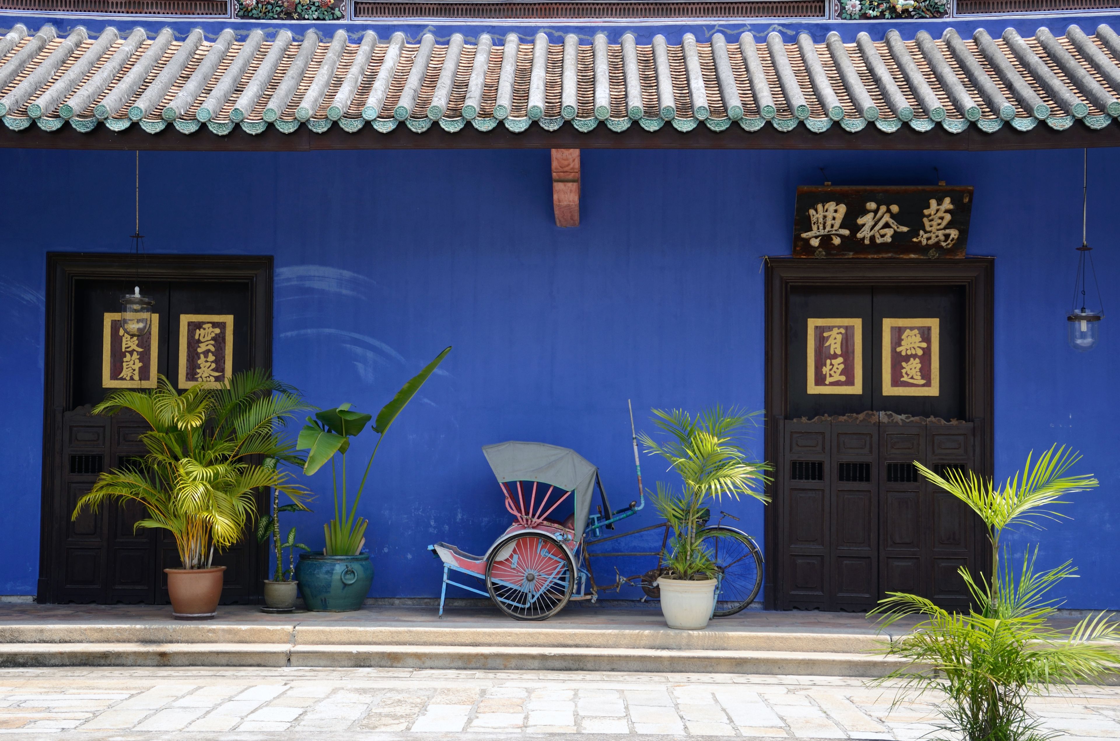 A traditional building with a blue facade, two wooden doors with gold plaques, and a bicycle parked in front.
