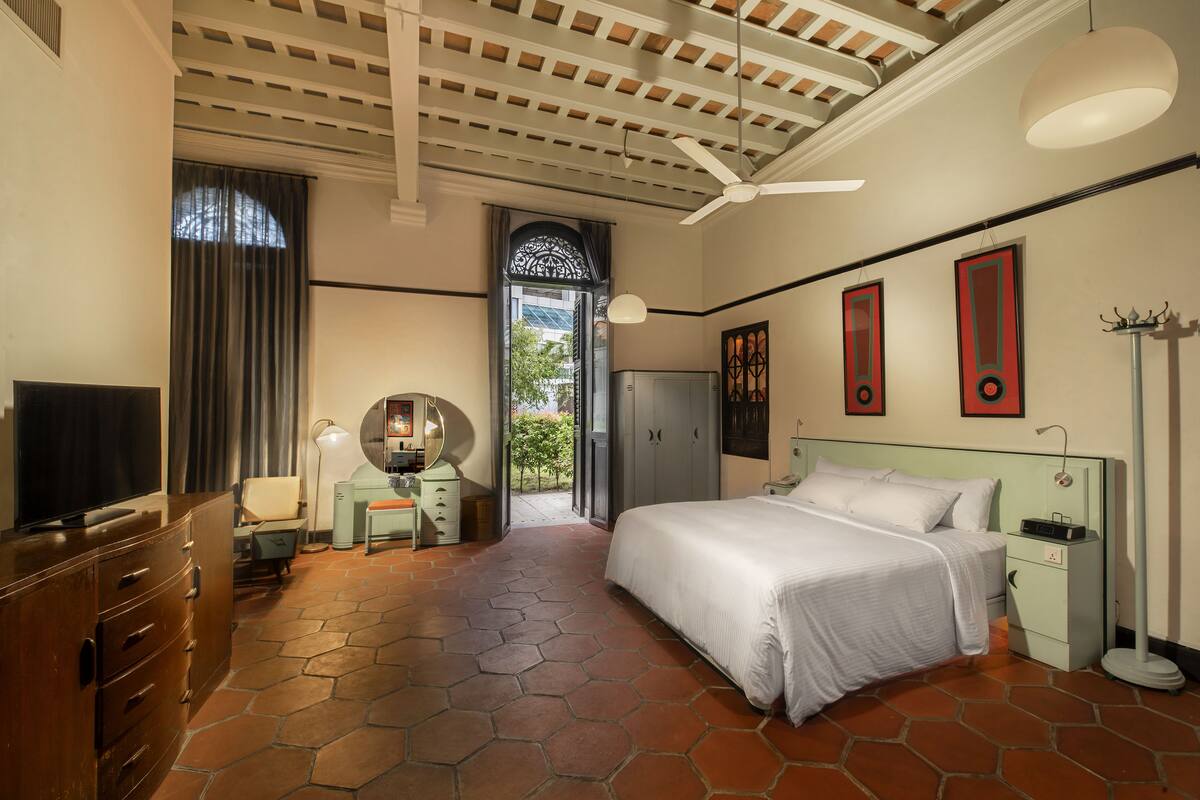 A bedroom with a bed, a desk, a television, and a ceiling fan.