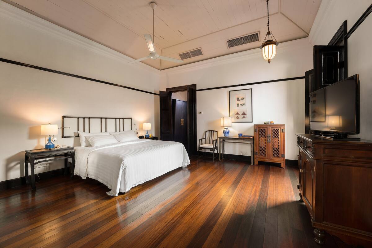 A hotel room with a large bed, a desk with a chair, a television, and a wardrobe.