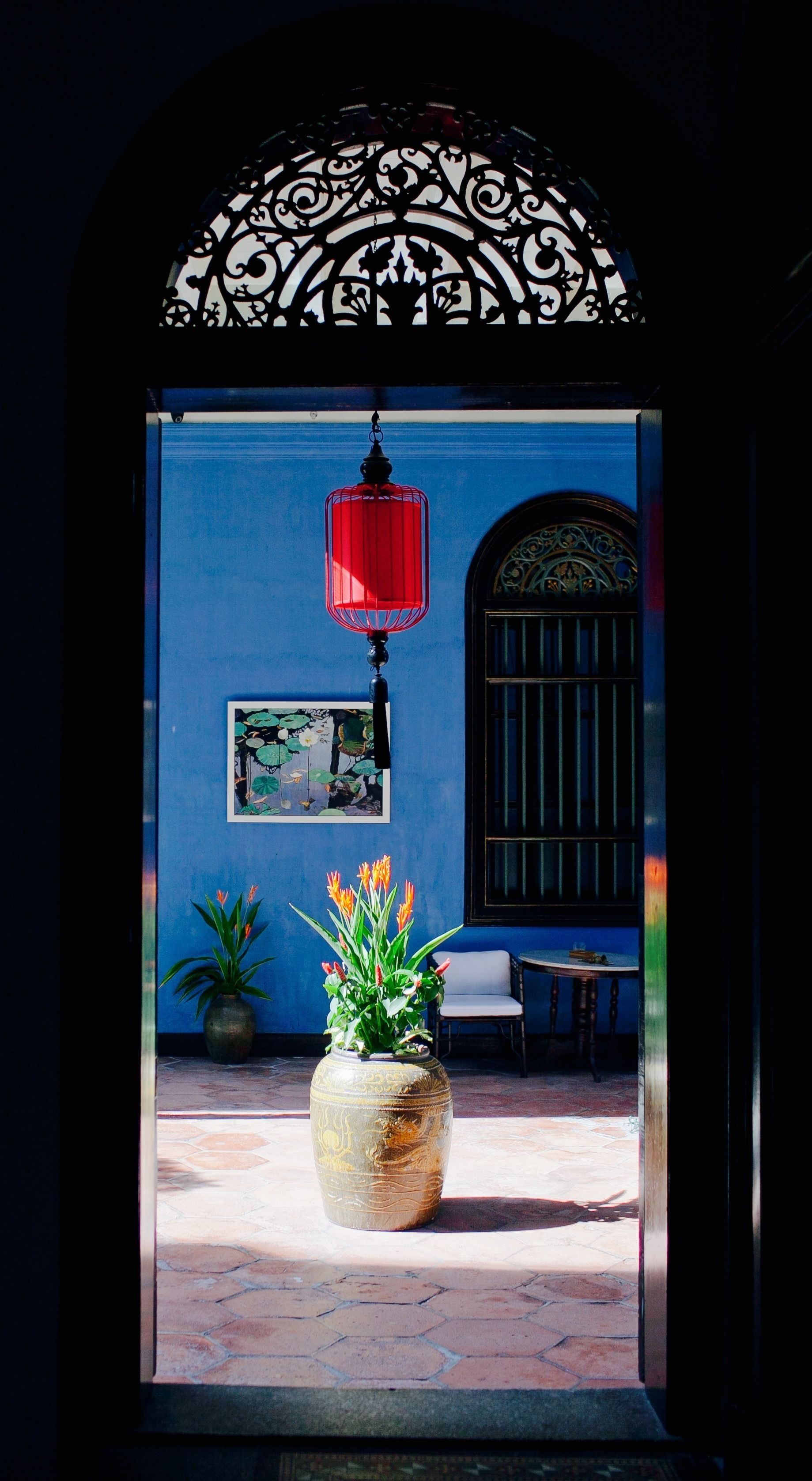 Une entrée agrémentée d’une arche décorative en métal, d’une lanterne rouge, d’une grande plante en pot et d’un tableau encadré au mur.