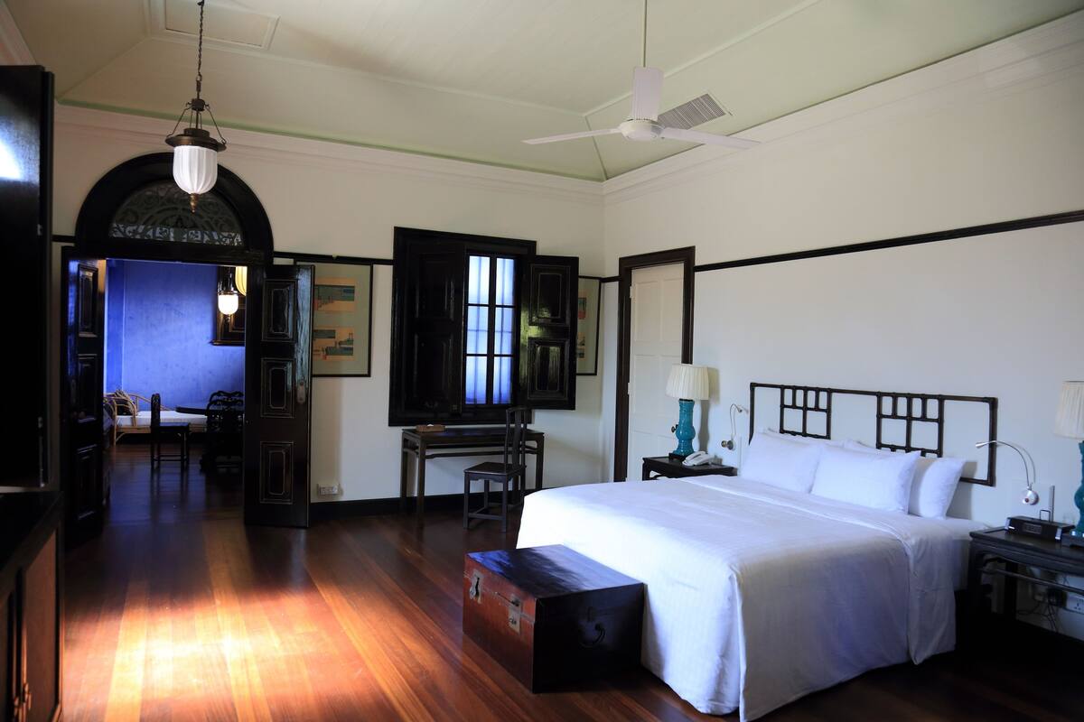 A hotel room with a bed, desk, chair, and a desk lamp.