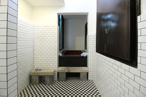 Un baño pequeño y estrecho con paredes de azulejos blancos y un piso a cuadros blanco y negro. Hay un banco y un perchero.