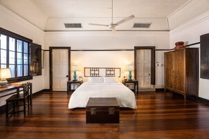 Un dormitorio amplio con una cama grande, piso de madera, ventilador de techo y un escritorio con silla.