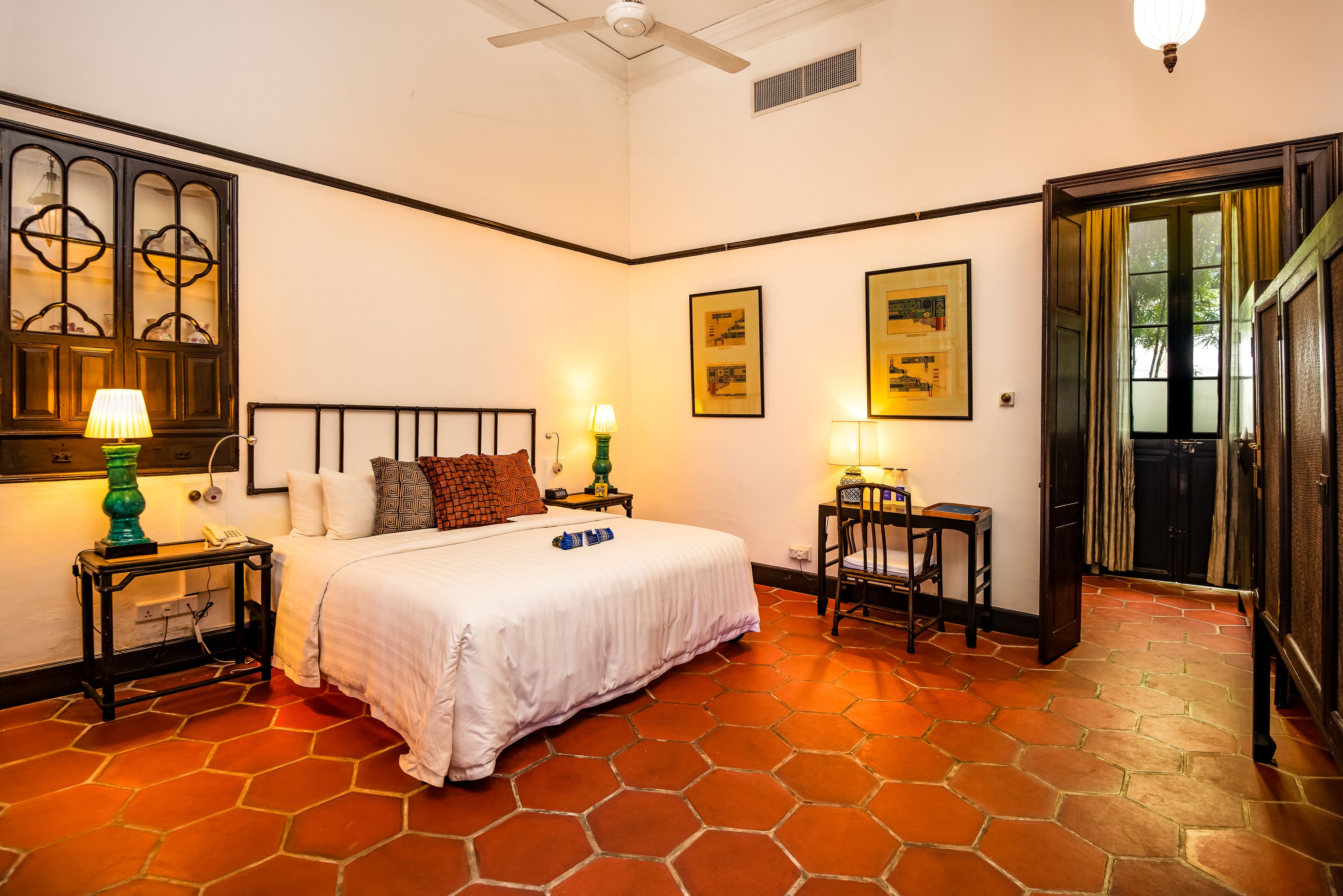 Un dormitorio con cama, dos mesitas de noche con lámparas, una silla y una puerta que da a otra habitación.