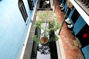 A narrow alley with a tree in a planter, tiled walls, and a small water feature.