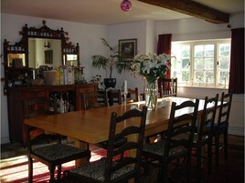 A dining room with a wooden table and chairs, a vase with flowers, and a window with curtains.