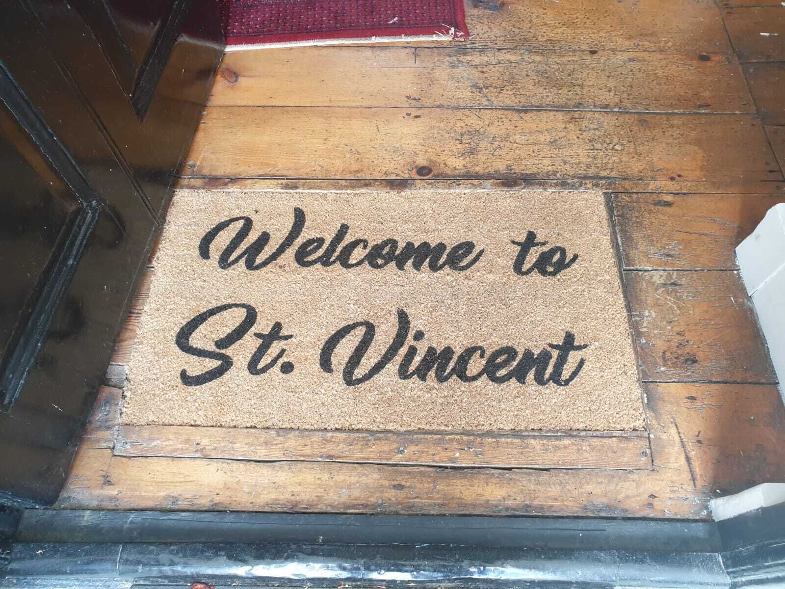 Un felpudo con el texto 'Welcome to St. Vincent' sobre un piso de madera.