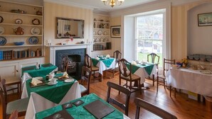 A dining room with multiple tables set for meals, a fireplace, and shelves with dishes and books. - St Vincent Guest House (Lynton)