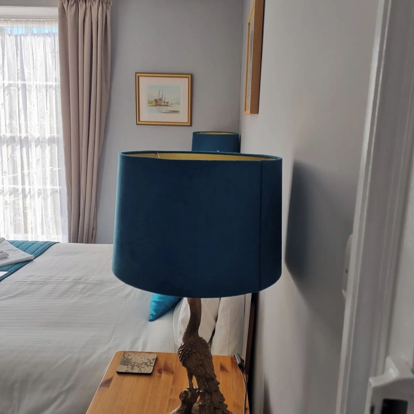 A bed with a blue blanket, a wooden nightstand with a lamp, and a framed picture on the wall.