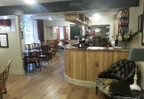 A cozy bar area with a wooden counter, seating with chairs, and a black leather couch. - The Wheatsheaf Inn (Kendal)