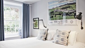 A bedroom with a large bed, a window with curtains, a wall-mounted lamp, and a poster of Kendal from Oxenholme. - The Wheatsheaf Inn (Kendal)