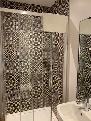 A bathroom with patterned tiles, a glass shower enclosure, and a white sink with a modern faucet. - The Wheatsheaf Inn (Kendal)