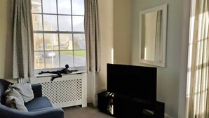 A room with a large window, a black TV stand, a blue sofa, and a radiator. - Olivers Guest House (Weymouth)