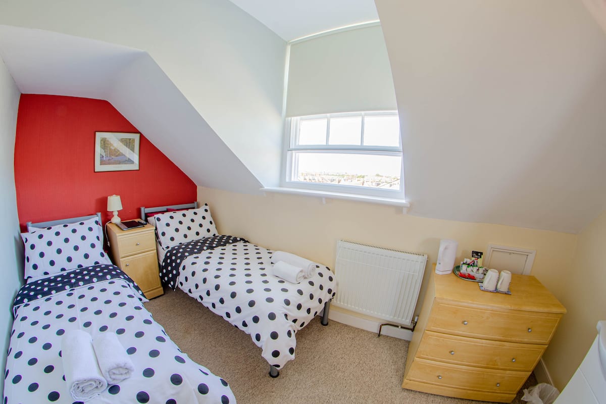 A bedroom with two beds, a dresser, a radiator, and a window with a view.