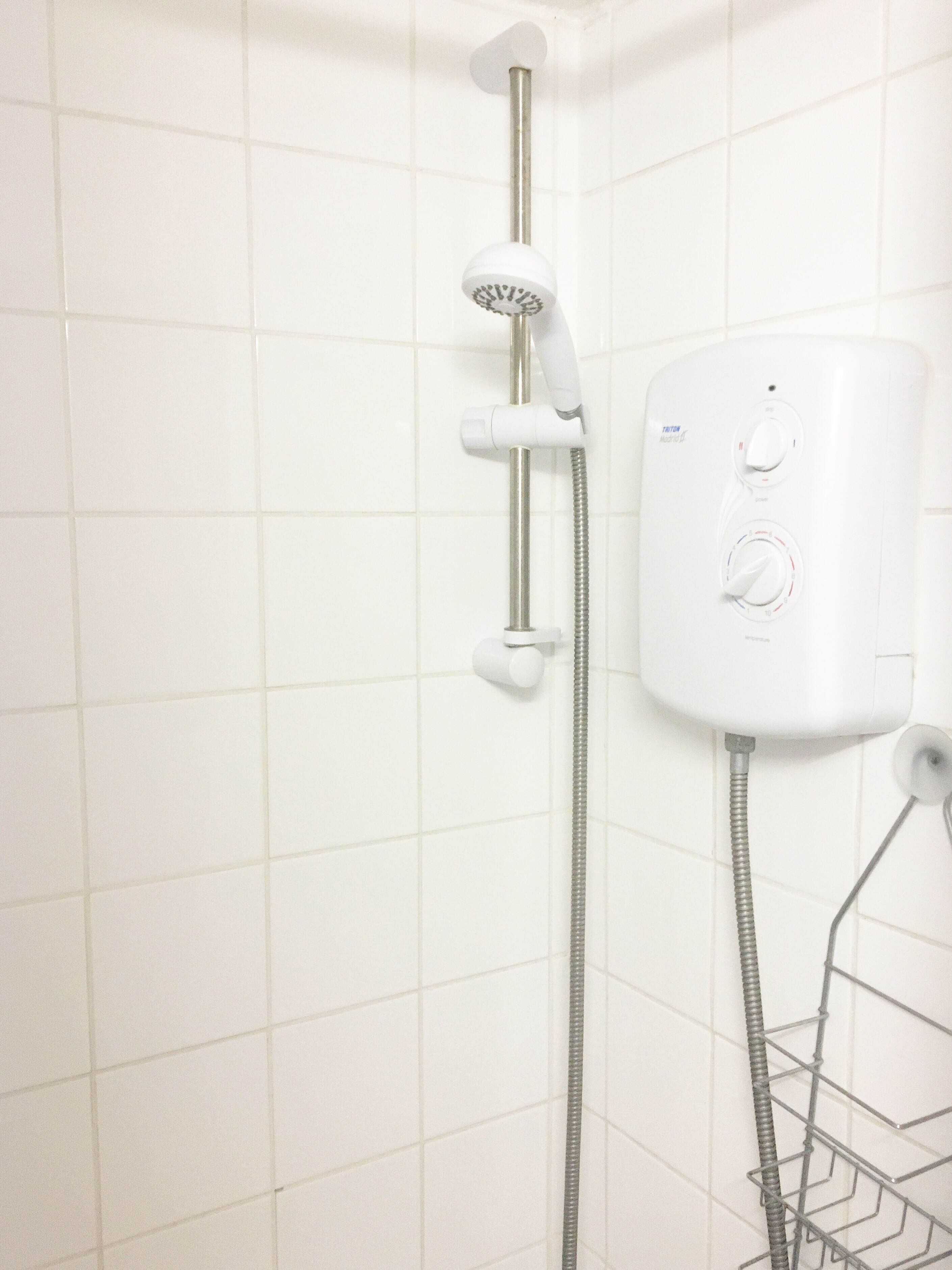 Une douche équipée d’un pommeau de douche à main et d’un panneau de commande fixé au mur.
