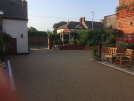 A residential backyard with a paved area, a small gazebo, and a brick wall with potted plants.