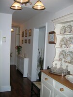 A kitchen with wooden cabinets, a white countertop, and a decorative backsplash. There is a hallway leading to another room with framed pictures on the wall.