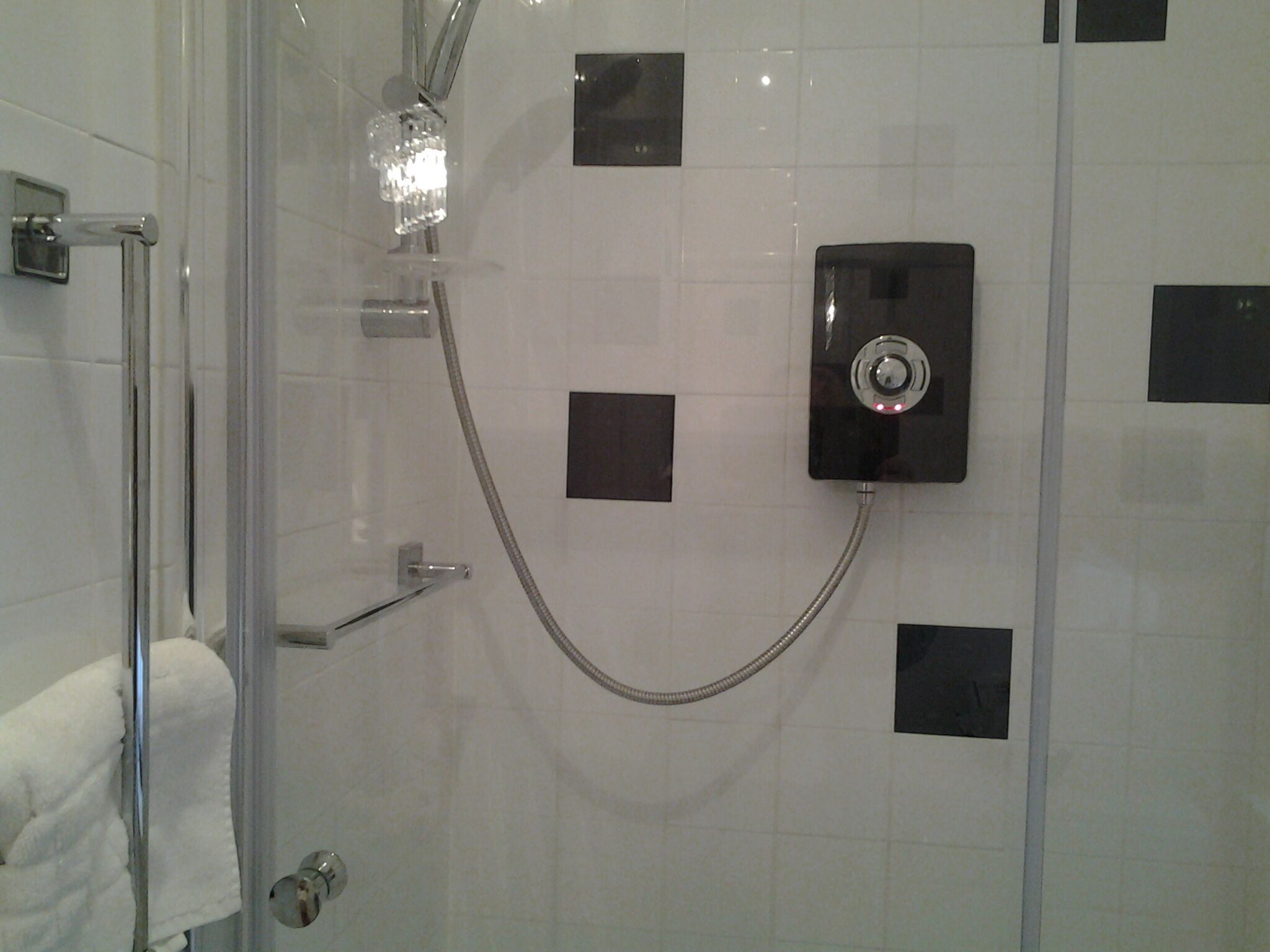 A shower with a handheld showerhead and a wall-mounted control panel.