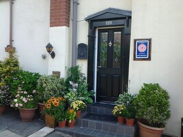 Uma porta preta com o número 120, um letreiro de Enjoy England e plantas em vasos na frente.